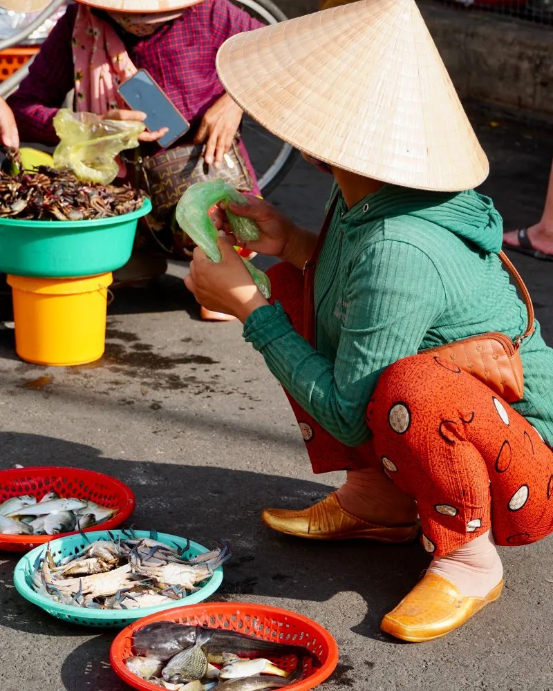 Người bán đội nón lá ngồi bên các thau hải sản ở chợ sáng